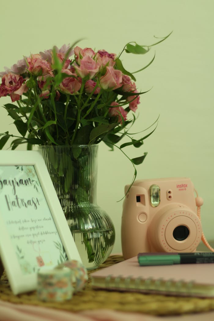 A delightful desk arrangement with pink roses in a vase, a framed quote, and a vintage-style camera for a cozy aesthetic.