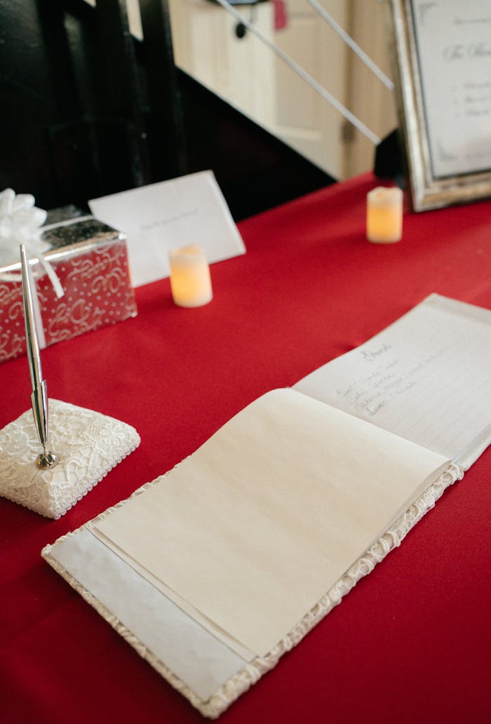 Elegant wedding guest book on a red tablecloth with decorative pen and candles.